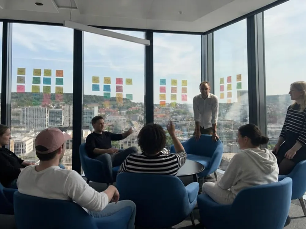 Team workshop in a glass corner office, sticky notes on the windows, Marcin facilitating